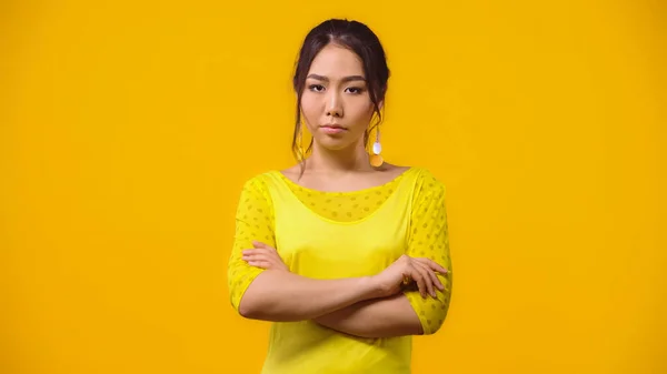 Недовольная азиатка, стоящая со скрещенными руками, изолированная на желтом — стоковое фото