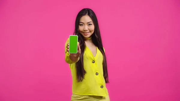 Счастливая азиатская женщина держит смартфон с зеленым экраном изолированы на розовый — стоковое фото