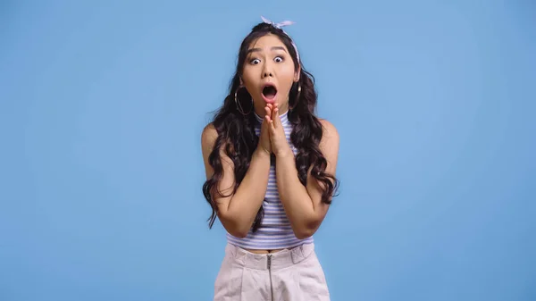 Shocked and young asian woman with opened mouth and praying hands isolated on blue — Stock Photo
