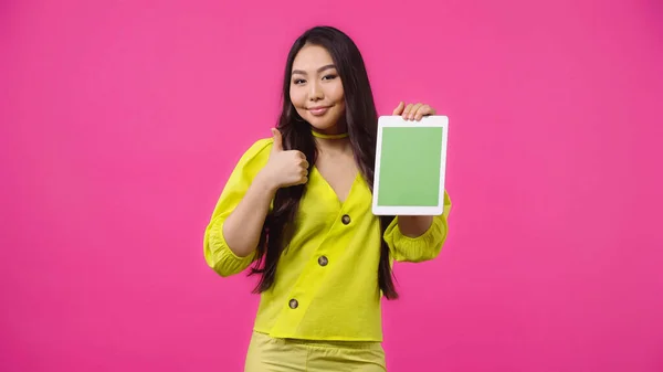 Весела азіатська жінка тримає цифровий планшет з зеленим екраном і показує, як ізольована на рожевому — стокове фото