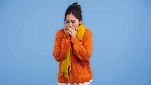 Enfermo asiático mujer en naranja suéter y bufanda toser aislado en azul - foto de stock