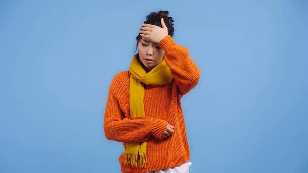 Malato asiatico donna in arancio maglione e sciarpa toccare fronte isolato su blu — Stock Photo