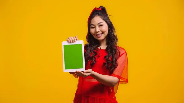 Heureux asiatique femme tenant numérique tablette avec écran vert isolé sur jaune — Photo de stock