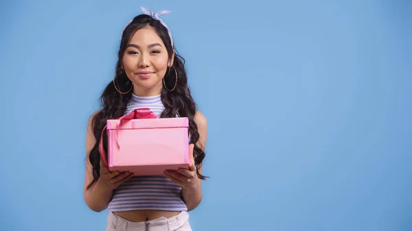 Щаслива молода азіатська жінка тримає загорнуту подарункову коробку ізольовано на синьому — стокове фото