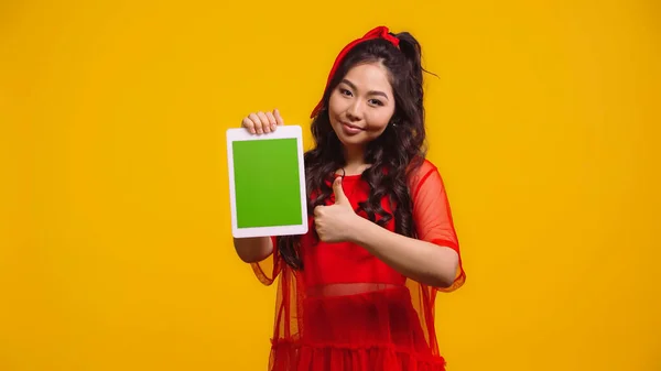 Весела азіатська жінка тримає цифровий планшет з зеленим екраном і показує, як ізольована на жовтому — стокове фото