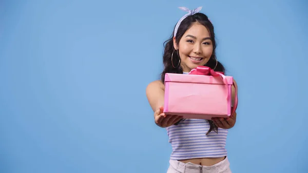 Positive asiatische Frau gibt verpacktes Geschenk isoliert auf blau — Stockfoto