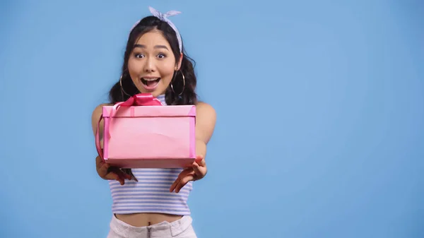 Aufgeregte junge asiatische Frau hält verpacktes Geschenk isoliert auf blauem Grund — Stockfoto