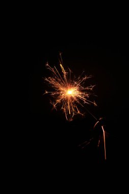 Noel ve Yeni Yıl partisi maytapları siyah arka planda, neşeli kıvılcım efektleriyle parıldıyor, ince film tahılları, sıcak altın tonları, bokeh ışıkları, klasik atmosfer ekleme sesi.