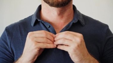 Polo tişörtünü ilikleyen eller tam olarak değil. Renkli bir polonun yakasını nasıl ilikleyeceğinin yakın çekimi. Poloshirt yakasını düzelten adam üst düğmeyi açıyor. Rahat ve resmi giyinmiş hissediyorum..