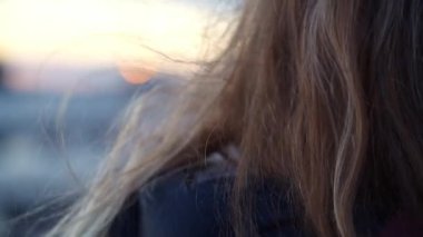 Rüzgarla savrulan sarı saçlar. Sarışın kadın gün batımını seyrediyor ve akşam meltemiyle okşanıyor. Hareket eden saçlara yakın çekim.