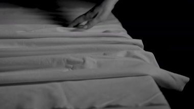 Kızın eli nazikçe çarşafı okşar. Genç bir kadının parmakları bir masanın üzerindeki kumaşın kıvrımlarına dokunur. Siyah arkaplanı olan dramatik siyah beyaz görüntüler..