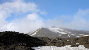 Volkanın tepesindeki bulutların zamanlaması. Kışın büyük volkan Etna. Aktif fümerollü sülfür ve gaz. Volkanik arazi, kar ve rüzgarlı bulutlar.