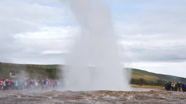 Strokkur, İzlanda - 09 22 2023: Ağır çekimde büyük gayzer patlaması. Turistler yerden gelen sıcak suyun görkemli akışını izliyorlar. Efendim, kaplıca fışkırıyor. 4k stok görüntüsü.