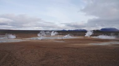Nmafjall Jeotermal Alanı. Turistler dumanı tüten fümeroller ve kaynamış çamur tencereleri arasında gezinirler. Müstehcen volkanik manzara manzarası. Sülfürlü çamur yayları, solfataralar ve buhar kaynakları. 4k ağır çekim
