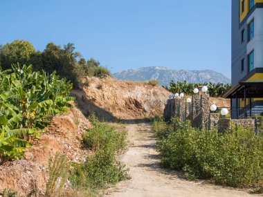 ALanya, Turkey - 27 Ekim 2022. Muz bahçesi olan yüksek bir konutun önündeki toprak yol.