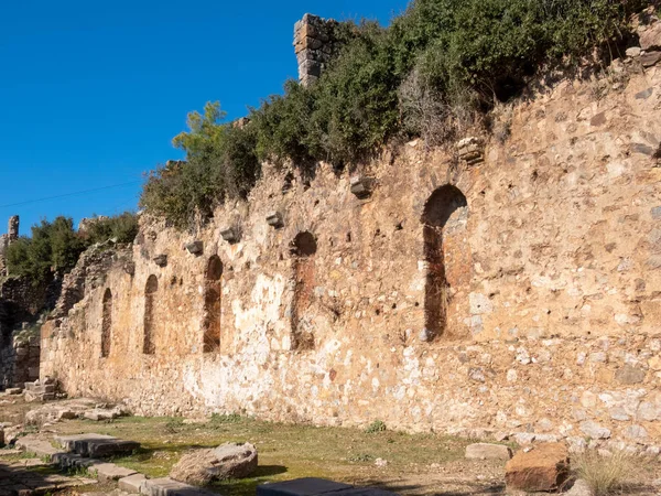 The ruined wall of antique building with several niches, overgrown with shrubs. The ancient city of Syedra, South Turkey, on a sunny day
