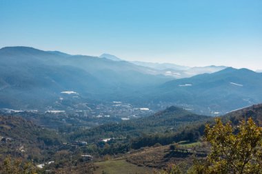 Güneşli bir günde, arka planda sonbahar renklerini gösteren dağlarla bir Akdeniz vadisi.