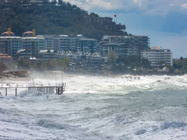 stock image Alanya, Turkey - Mar 23, 2023. Rough waves crashing into the coast with various buildings situated nearby on the shore. Stormy Mediterranean sea.