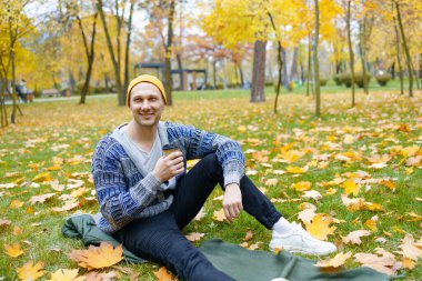 Güz parkında sabah kahvesi içip yürüyen orta yaşlı, yakışıklı, sakallı adam..