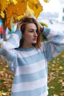 Süveter giyen kızıl saçlı genç kadın parkta yürüyor. Günbatımında gösterişli kızıl saçlı bir kadının sonbahar güzel portresi.