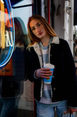 Hafif makyajlı genç bayan turist gece megalopolisine karşı renkli neon ışıklarıyla barın yanında duruyor..