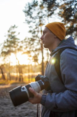 Genç fotoğrafçı ormanda fotoğraf çekiyor. Büyük profesyonel kameralı fotoğrafçı..