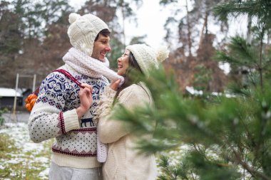 Mutlu çift kış ormanlarında eğleniyor. Kış tatilinde mandalina havası. Beyaz kazaklı duygusal genç çift kış ormanlarında yürürken eğleniyor..