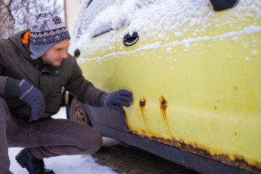A man shows rust on a car door from winter reagents. Close-up, selective focus on rust and hand.