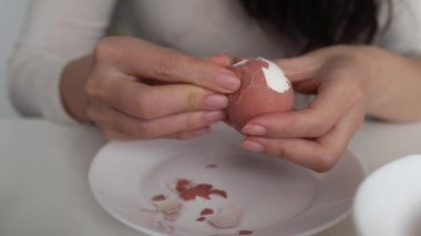 Dişi eller, kaynamış bir yumurtanın kabuğunu koyu ahşap bir arka planda temizler. Yemek hazırlığı.