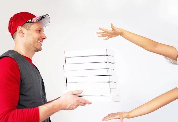 Photo of happy delivery man in red t-shirt and cap giving food order and holding many pizza boxes isolated on white background