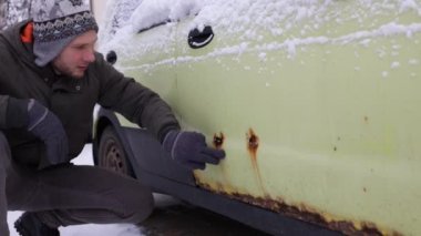 A man shows rust on a car door from winter reagents. Close-up, selective focus on rust and hand.