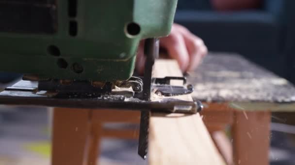 電動ジグソーを手にした大工さんの手が木を切り落とした 木を切るためにフレットソーを使う男性の手 大工は家の工房でジグソーで木を切る — ストック動画