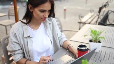 Serbest çalışan bir kadın açık havada bilgisayarla halka açık bir Wi-Fi 'a bağlı çalışırken kahvesini içiyor. Şık bir öğrenci kız şehirde online çalışıyor..