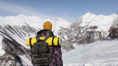 Kışın dağlarda sırt çantası takmış, karla kaplı duran bir adamın arka görüntüsü. Seyahat ve aktif yaşam tarzı kavramı.