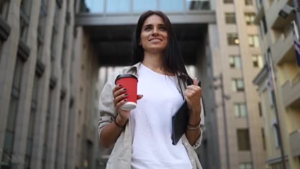 Tablet Kahve Bardağıyla Binaları Arasında Yürüyüp Neşeyle Gülümseyen Başarılı Genç — Stok video