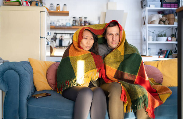 Couple cold on sofa at home with winter coat in a blanket.