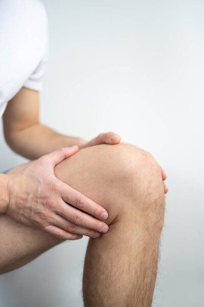 Young man suffering from knee pain on light background. Health care concept
