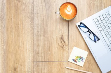 Work from home. work desk with laptop, blank notepad, coffee cup and pen on wooden table. Flat copy space top view.