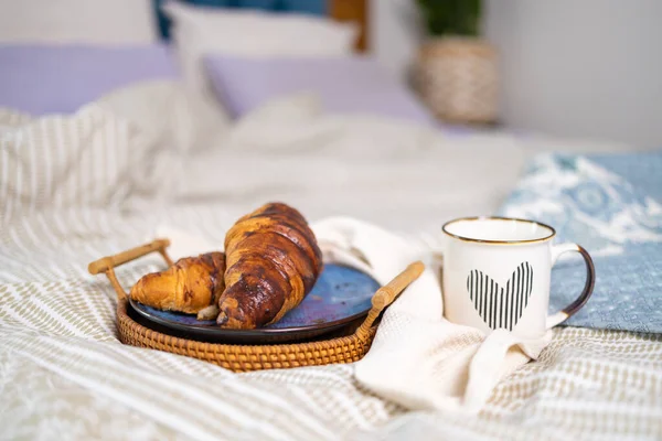 breakfast, cozy, morning, holidays and winter concept - cozy bedroom with cup of coffee and croissant on wooden board in bed at home