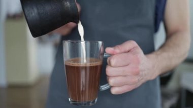 Close-up barista waitress pouring milk into hot melted chocolate.