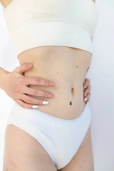 Flat female belly with moles. Beautiful body with birth marks of young woman isolated on gray studio background. Fit, healthy and slim authentical body. Natural beauty, treatment, healthcare.