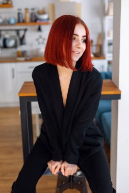 Pretty woman in jacket looking away while sitting on sofa at home