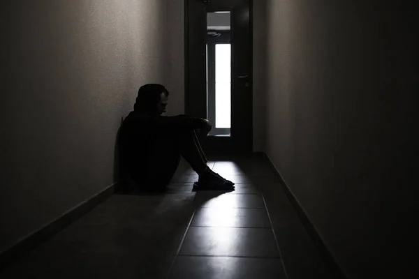 Silhouette of a depressed man sitting on the walkway of an apartment building. Sad man, crying, drama, lonely and unhappy concept.