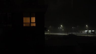 Falling snow in residential area at night. City courtyard night view in blizzard. Night town street with burning street lamps and snow covered parked cars during snowing