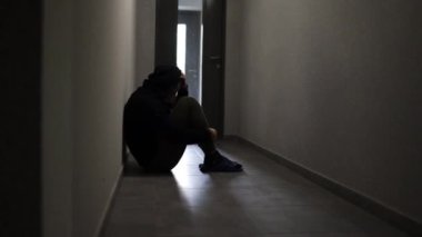 Depresyonda olan bir adamın silueti bir apartmanın geçidinde oturuyor. Üzgün adam, ağlayan, dram, yalnız ve mutsuz konsept.