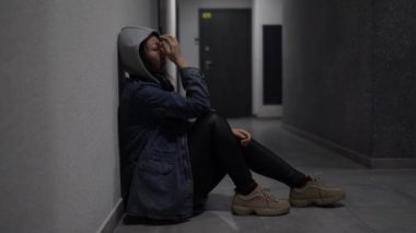 Silhouette of a depressed woman sitting on the walkway of an apartment building. Sad woman, crying, drama, lonely and unhappy concept.