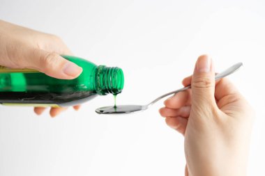 Hand pouring medicine or antipyretic syrup from bottle to spoon. healthcare, people and medicine concept.