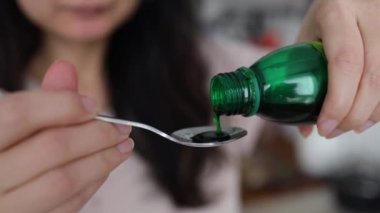 Sağlık, insan ve tıp konsepti - Asyalı kadın şişeden kaşığa ilaç ya da antipiretik şurup dolduruyor