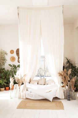Bed with pillows, wooden furniture, plants in pots, an armchair and curtains on large windows in a cozy bedroom interior, nobody, apartment, panorama, free spac