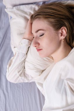 Calm serene beautiful young lady wears pajamas, lying down in a dream, relaxing sleep in a cozy white bed on a soft pillow covered with a blanket, enjoying a good healthy sleep concept, top view